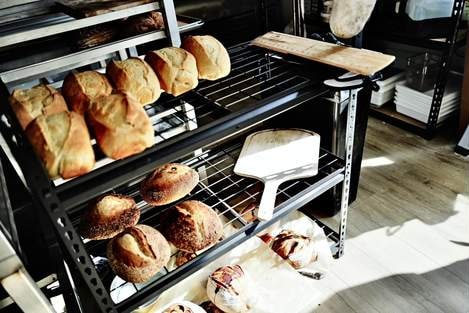 Loaves cooling on wire racks in the bakery, a wooden peel beside them