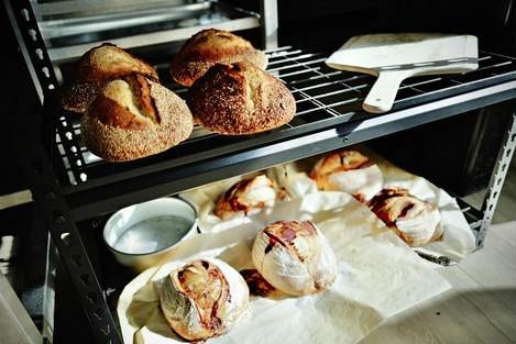 Seeded loaves on a wire rack above scored loaves resting on parchment