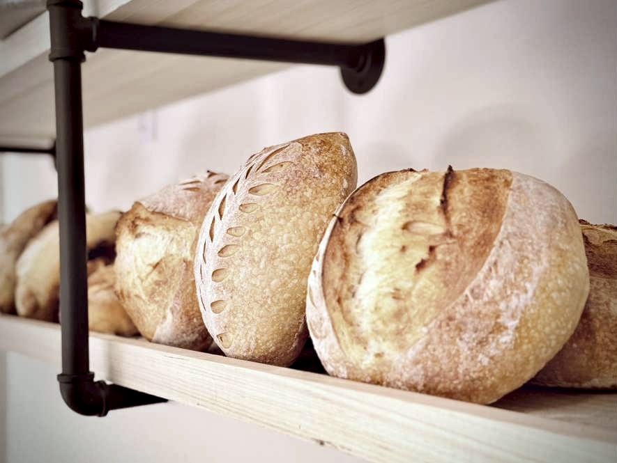 Sourdough loaves on a wooden shelf, scored with a wheat pattern